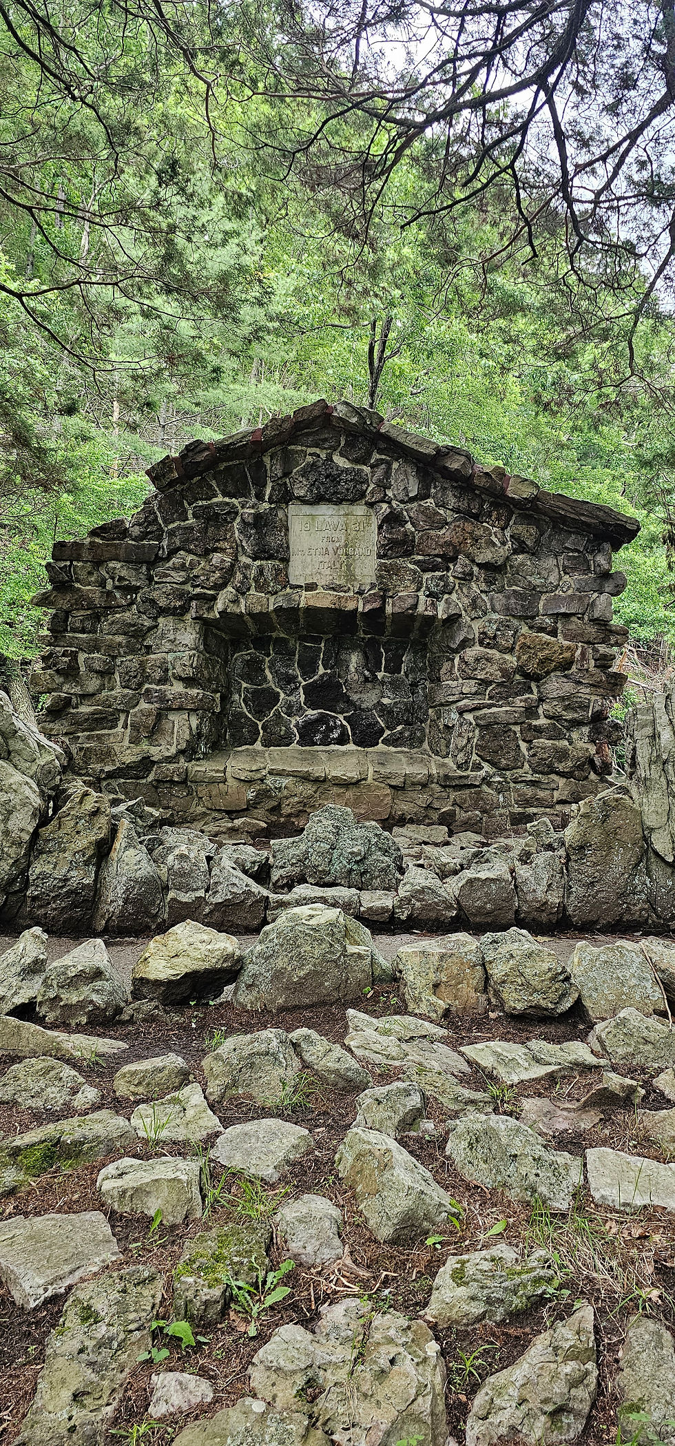 Stone structure in a forest, surrounded by rocks and greenery; inscription on the stone. The mood is serene and natural.