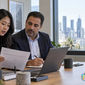 Two diverse compliance professionals in an Australian office reviewing an authorized background screening document and laptop, with Sydney Harbour Bridge in the background.