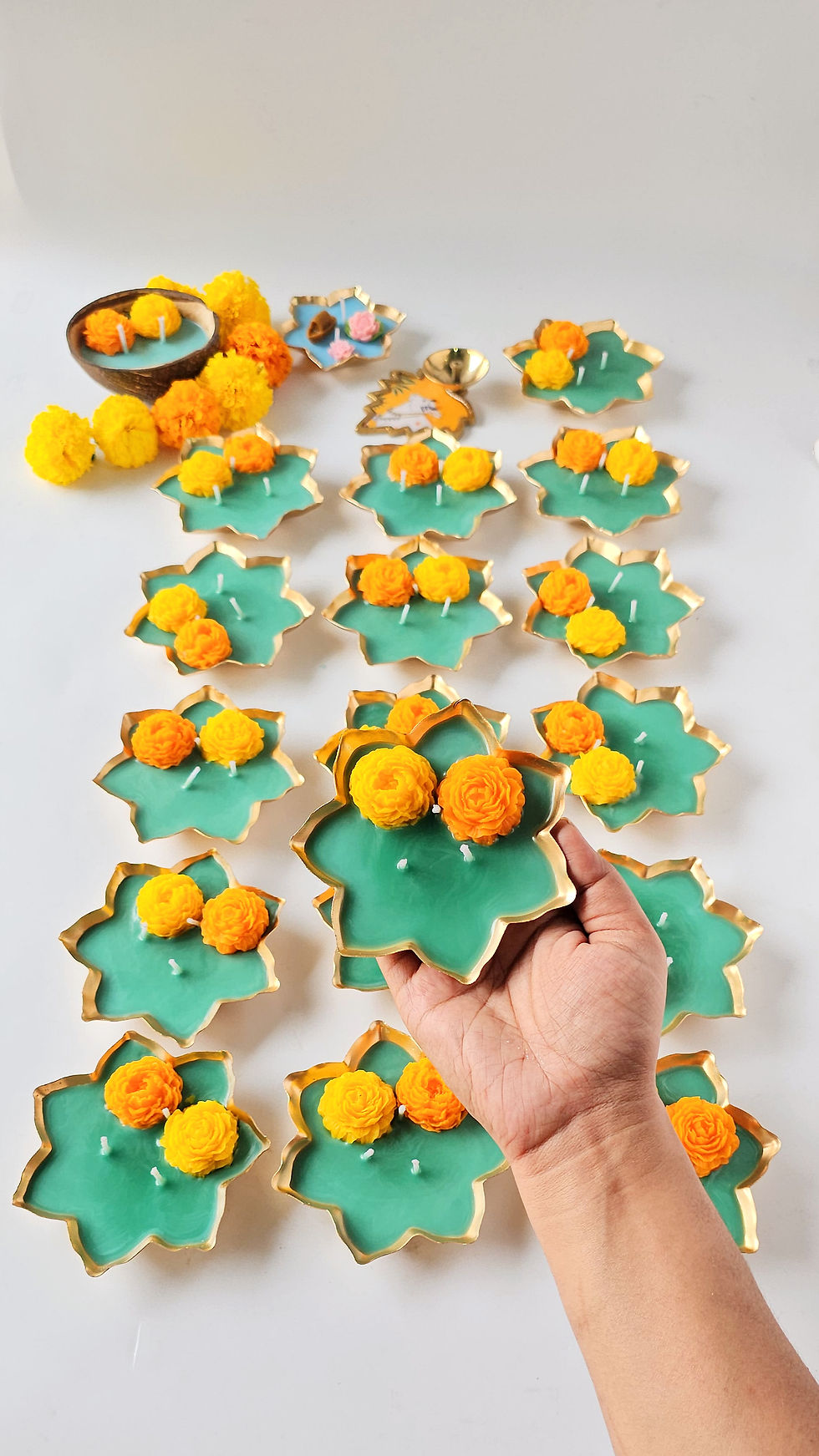 Hand arranging soy wax marigold urli candles in teal and gold on a table