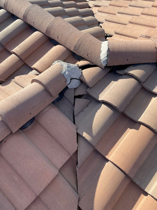 “Close-up of a roof with cracked and broken clay tiles, exposing the underlayment and increasing risk of water intrusion.”