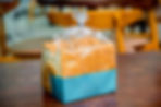A loaf of sliced ultra processed UPF bread in clear plastic and blue wrapping sits on a wooden table. Background shows blurred chairs in a casual setting.