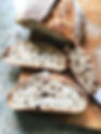 Sliced sourdough bread on a wooden board. The crust is golden and the interior is airy and soft. Set on a speckled countertop.