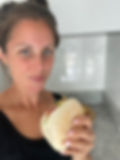 Corporate nutritionist holding a non UPF roll, standing in a modern kitchen with grey countertops. She has a subtle smile and wears a black top.