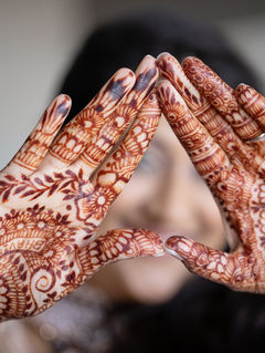 Hands with intricate henna designs form a triangle. The background is blurred, focusing on the detailed patterns and vibrant bangles.