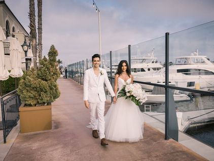Bride and groom walk down a dock ramp at their yacht wedding, with a romantic waterfront backdrop.