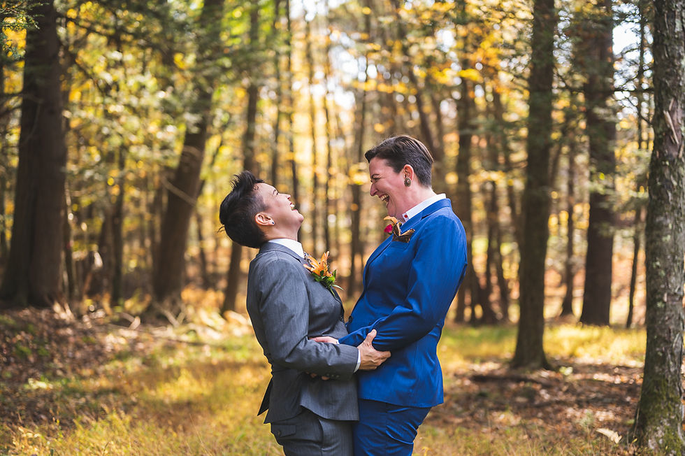 A queer couple laughs joyously on their wedding day with fall forest behind them. Photographed by queer LGBTQ+ photographer Lindsay Ladd of Baltimore. 