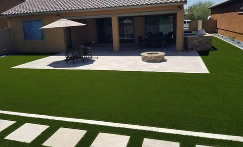 Modern backyard patio with a stone fire pit and table and chairs with umbrella.  Flagstone walkway.  All surrounded with bright green artificial turf.