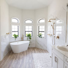 Luxury bathroom remodel in Ponte Vedra Beach by JHN Builders, featuring a freestanding tub, open shower with floor sloped to drain, white custom vanity cabinets, custom plumbing fixtures, tile flooring, and tile shower walls.