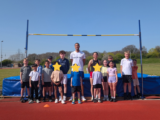 Children standing in front of the high jump with Olympian Tom Gale