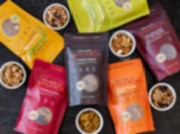 six varieties of buckwheat granola in 10oz bag size with ramekins of loose granola on black marble countertop