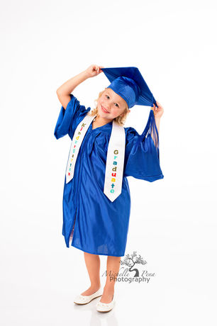 Child photography for a Kindergarten graduate she is wearing a blue cap and gown posed on a white backdrop.