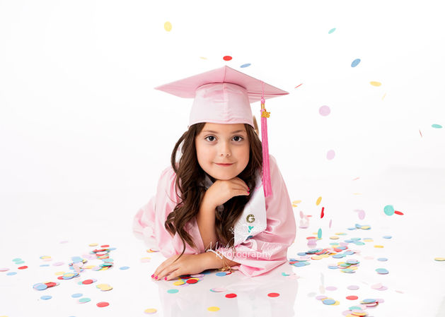 Child photography in Victoria,Texas with a little girl in a pink cap and gown. Fun colorful confetti is falling around her and above her.