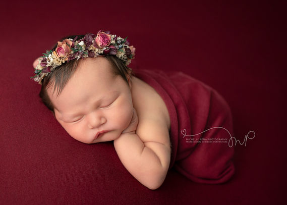 newborn photography session using burgundy swaddle and floral headband 