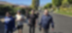 Six men walking together up a quiet residential street lined with palm trees, with desert mountains ahead of them.