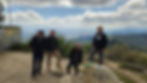 Four men posing on rocks at a mountain overlook, with a cloudy valley stretching out behind them.