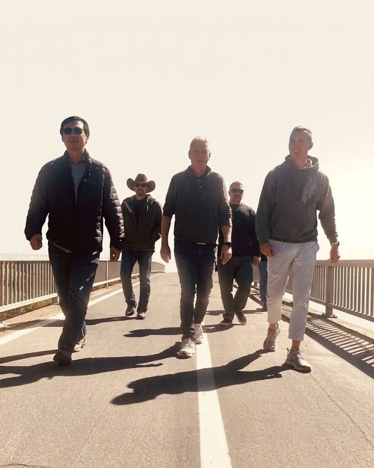 A group of men walking together across a bridge in bright morning light
