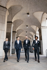 Groom and friends walking under the arches near NYC City Hall after the wedding ceremony