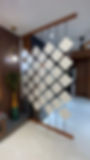 Modern interior with hanging white diamond panels as a room divider, wood accents, peacock-feather vase, and glossy floor.