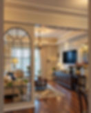 Elegant living room with cream sofa, chandelier, wall TV, and floral decor reflected in a large arched mirror.