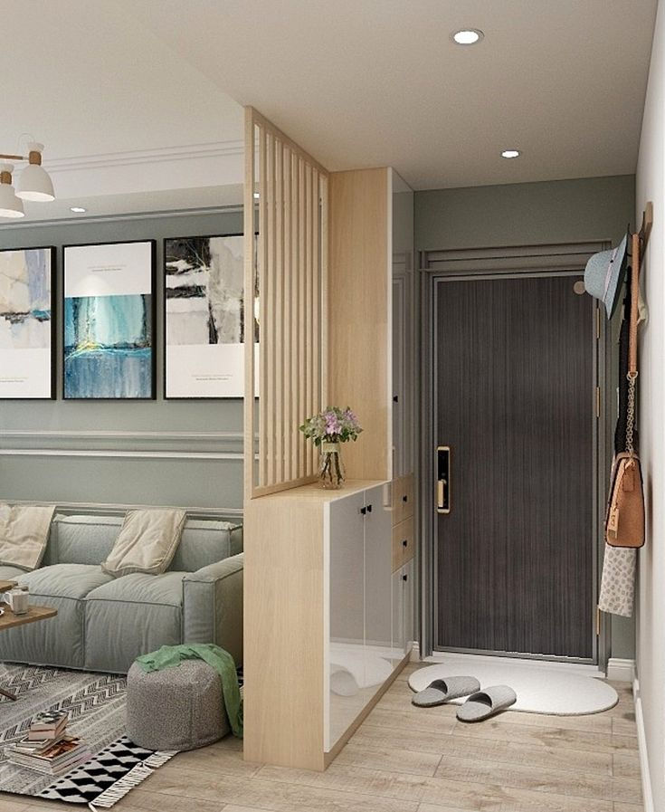Modern apartment entryway with dark door, white mat and slippers beside a mint sofa, art prints, and a small flower vase.