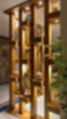 Wooden decorative room divider with recessed lights and gold ornaments in a warm lobby, with a leafy green plant in front.