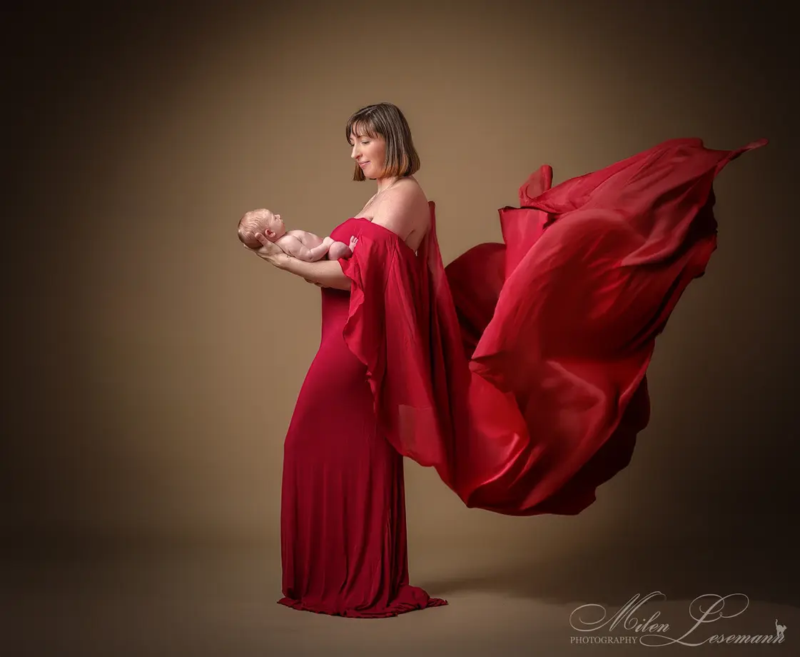 Mutter im roten Kleid hält Neugeborenes – künstlerische Neugeborenen Fotografie Berlin Studio Lesemann