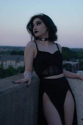 Woman in black outfit poses on a rooftop at dusk, looking away.