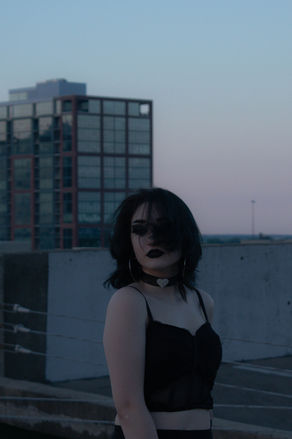 Woman in black clothing poses on a rooftop with cityscape background.