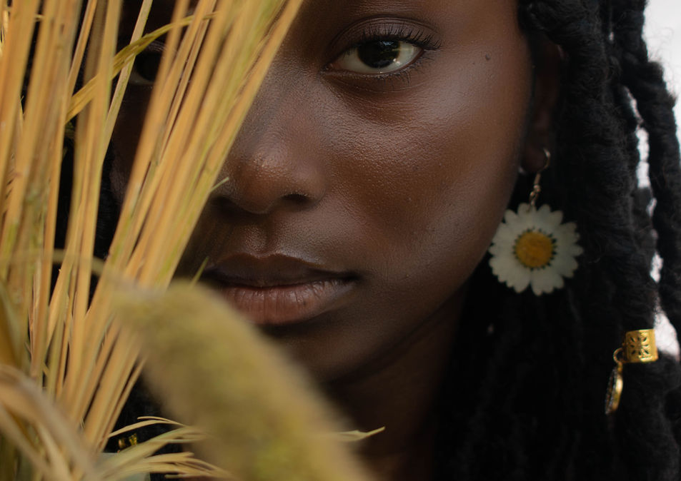 Young woman with dark skin and long braids, wearing daisy earrings.