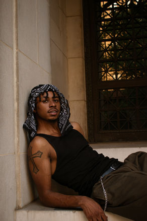 Young man with bandana leaning against a wall by a window