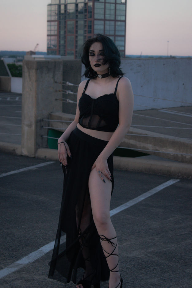 Woman wearing black dress posing on a rooftop with a tall building.