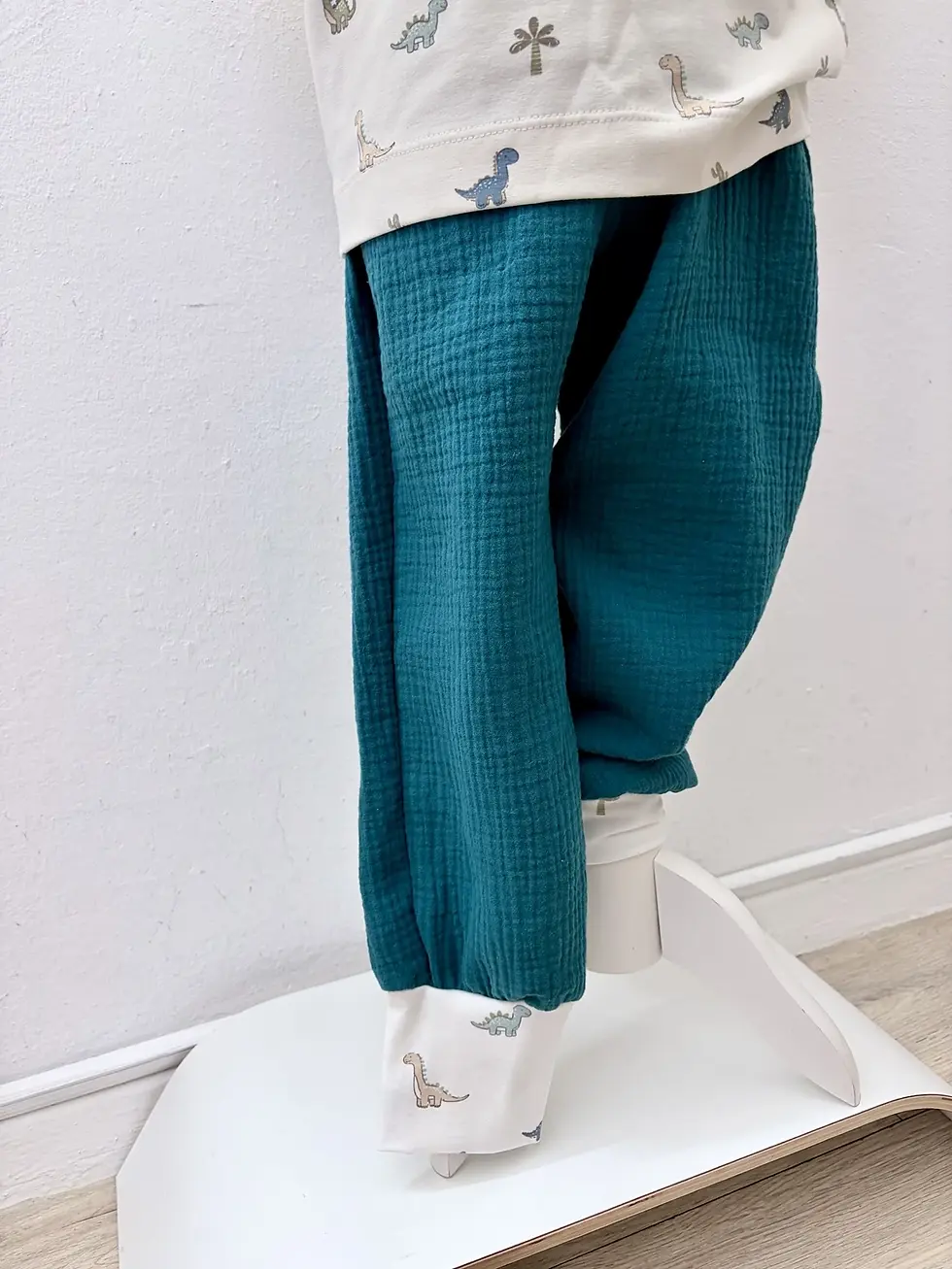 Miniaturbild: Studioaufnahme der petrolfarbenen Musselinhose Dino-Spaziergang, handgemacht in Hamburg für aktive Küstenkinder.