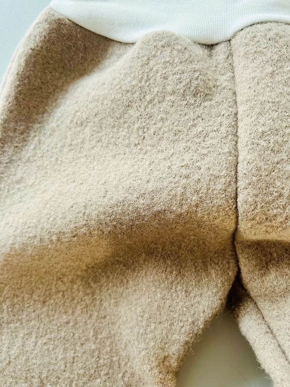 Miniaturbild: Detailaufnahme der beigen Wollwalkhose mit cremefarbenem Bündchen und Wal-Waschlappen, handgemachte Baby- und Kinderkleidung