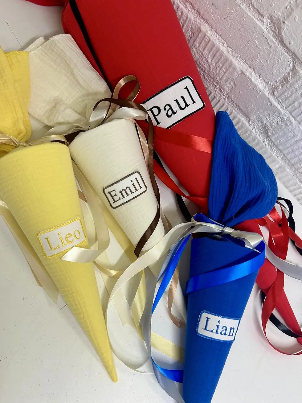 Miniaturbild: Mehrere personalisierte Musselin Schultüten in Gelb, Creme, Blau und Rot mit Namenspatch als Farb- und Gestaltungsauswahl.