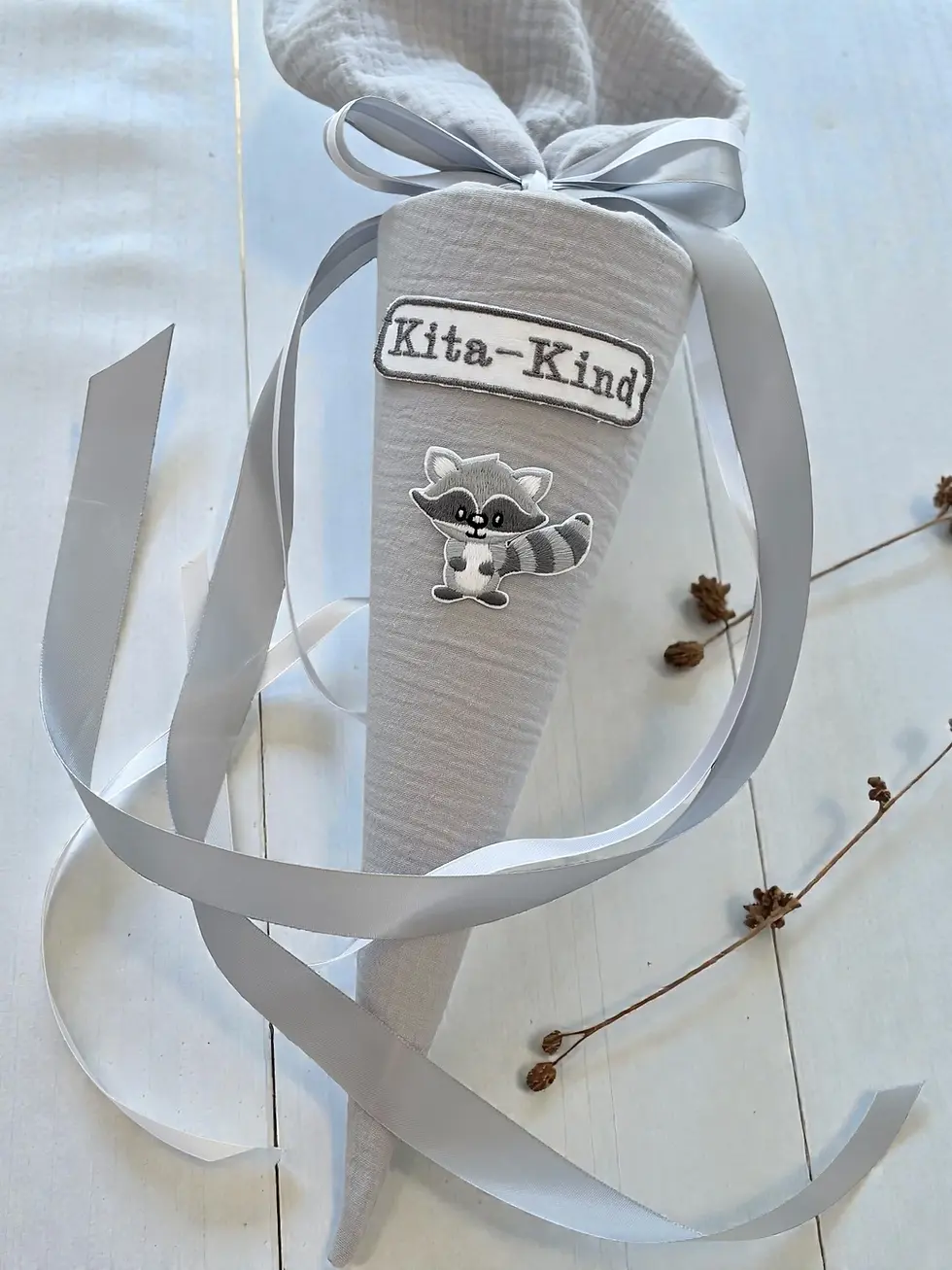 Miniaturbild: Kleine Kitatüte aus Musselin in hellem Beige-Grau mit Waschbär-Motiv und weichen Satinbändern. Ruhige skandinavische Stoffsch