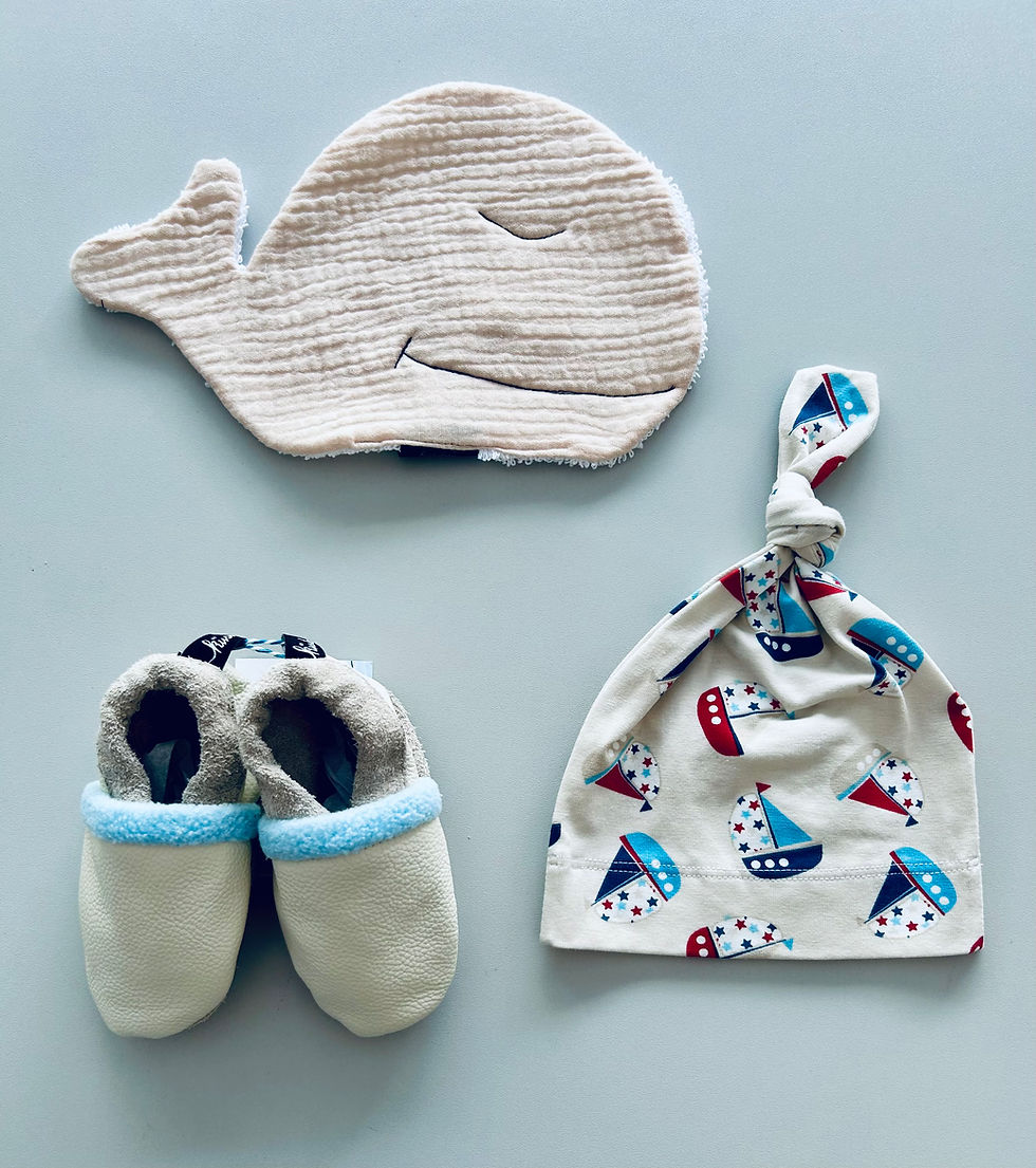 Miniaturbild: Cremeweiße Babypuschen aus Ökoleder mit einem Musselin Waschlappen in Walform und einer Knotenmütze in beige mit Segelbooten