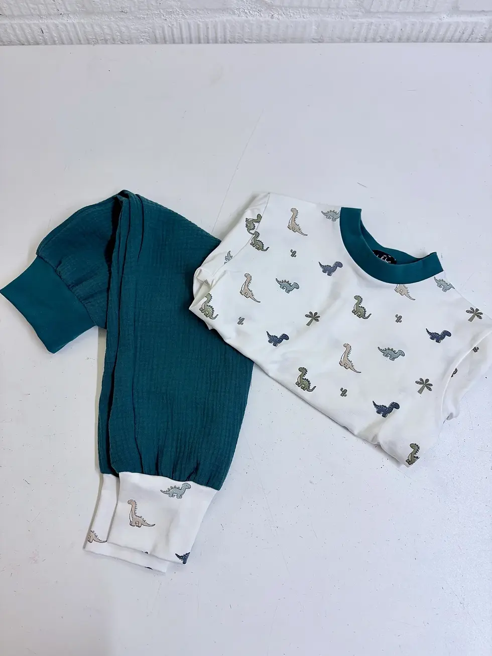 Miniaturbild: Flatlay vom Dino Kurzarmshirt aus OEKO-TEX Baumwolle. Handgemachtes Babyshirt von Küstenfieber® mit ruhigem Dinosaurier-Muste