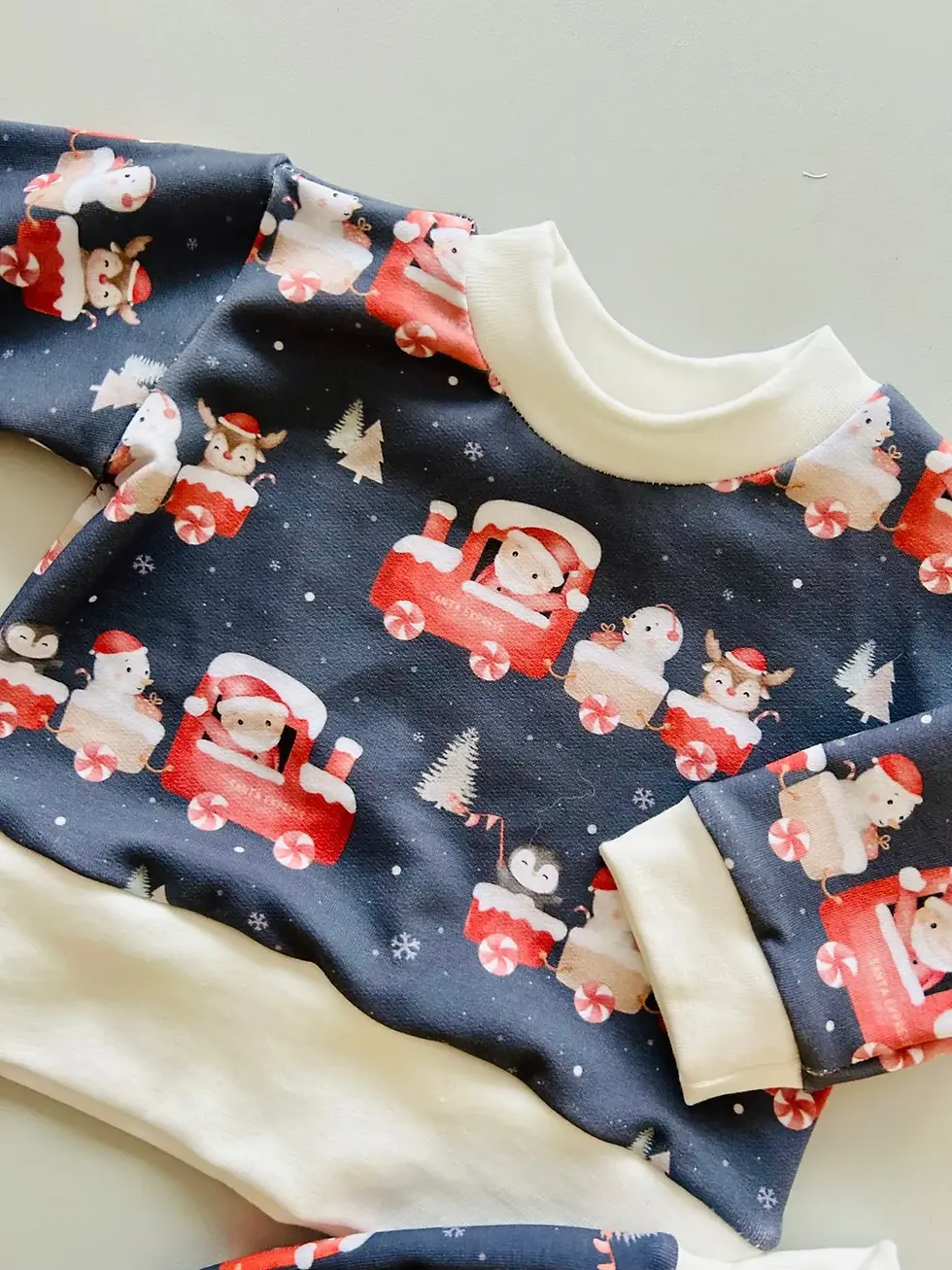 Miniaturbild: Weihnachtlicher Baby-Sweater, gefaltet präsentiert. Santa-Express-Motiv, dunkelblauer Hintergrund, weich und bequem.