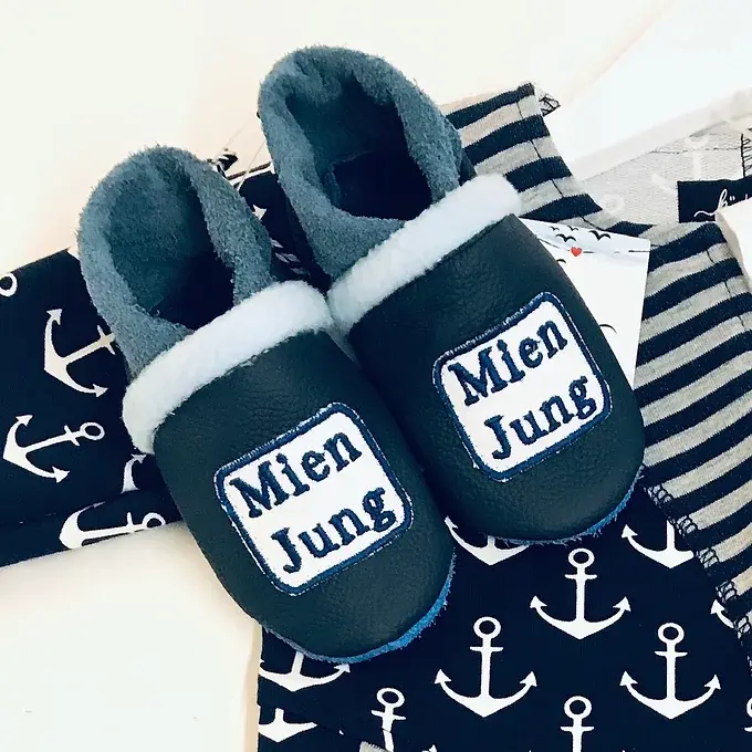 Handgemachte Lederpuschen für Babys mit „Mien Jung“-Stickerei in Blau und Hellblau.