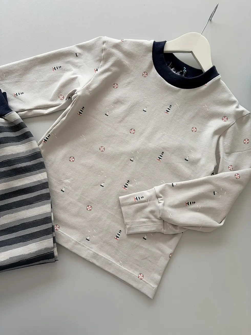 Miniaturbild: Beiges Kinder-Langarmshirt mit Leuchtturm-Motiv als Flatlay – schlichter maritimer Look, angenehm weich und hochwertig.