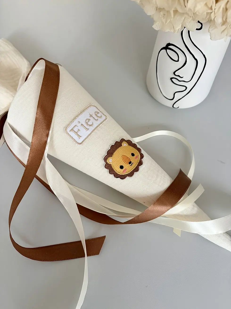 Miniaturbild: Personalisierte Musselin Schultüte in Creme mit Löwen-Applikation und harmonisch abgestimmten Satinbändern.