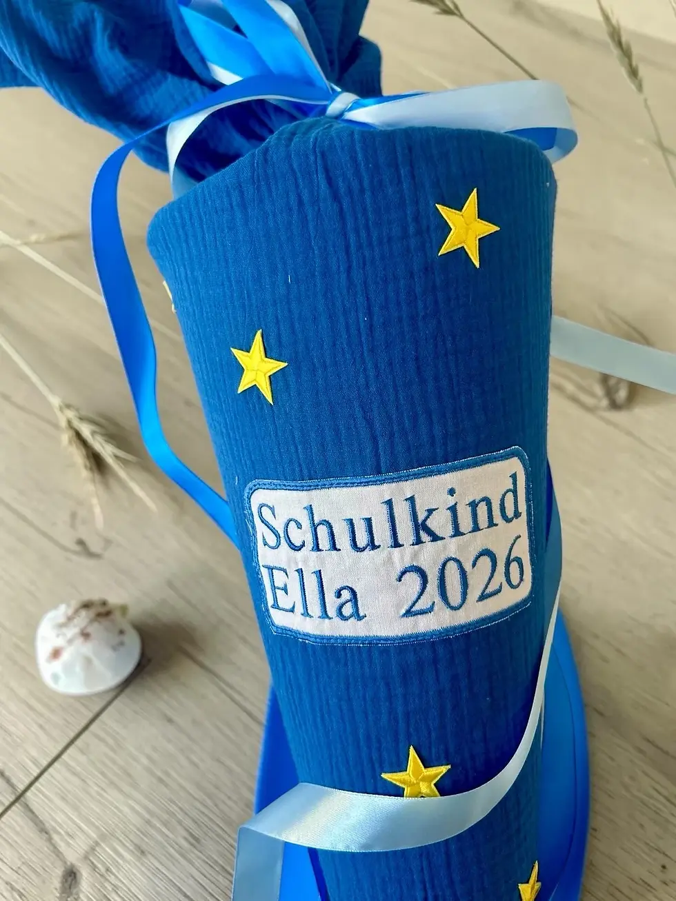 Miniaturbild: Nahaufnahme der Musselin-Schultüte „Sternenhimmel“ in Royalblau mit gelben Sternen, Namenspatch und Satinbändern.