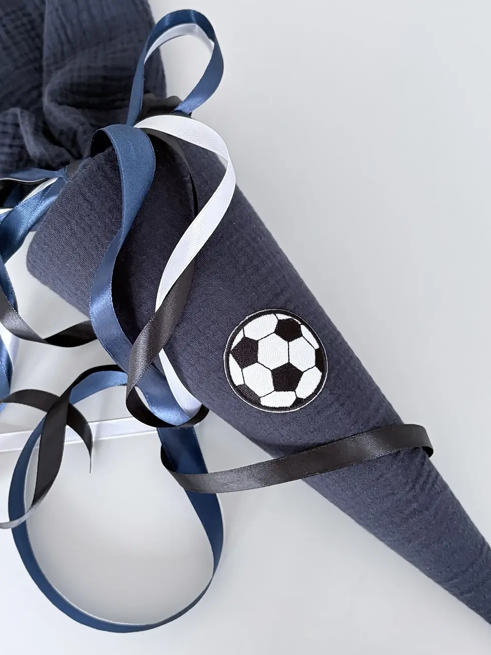 Detailaufnahme der anthrazitfarbenen Musselin Schultüte mit aufgenähter Fußball-Applikation und dekorativen Satinbändern.