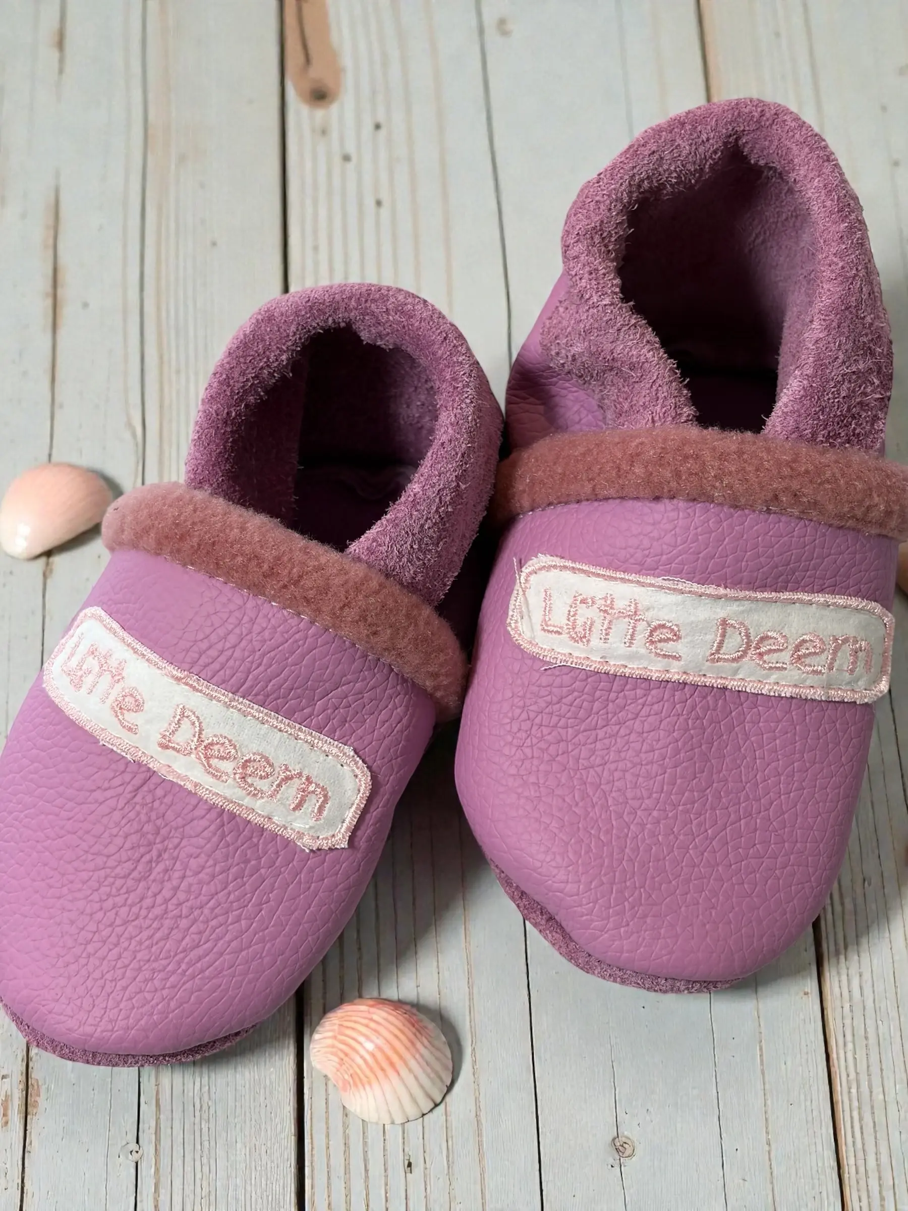 Rosa Lederpuschen aus weichem Ökoleder mit „Lütte Deern“-Stickerei auf heller Holzoberfläche fotografiert. Handgemacht in Ham