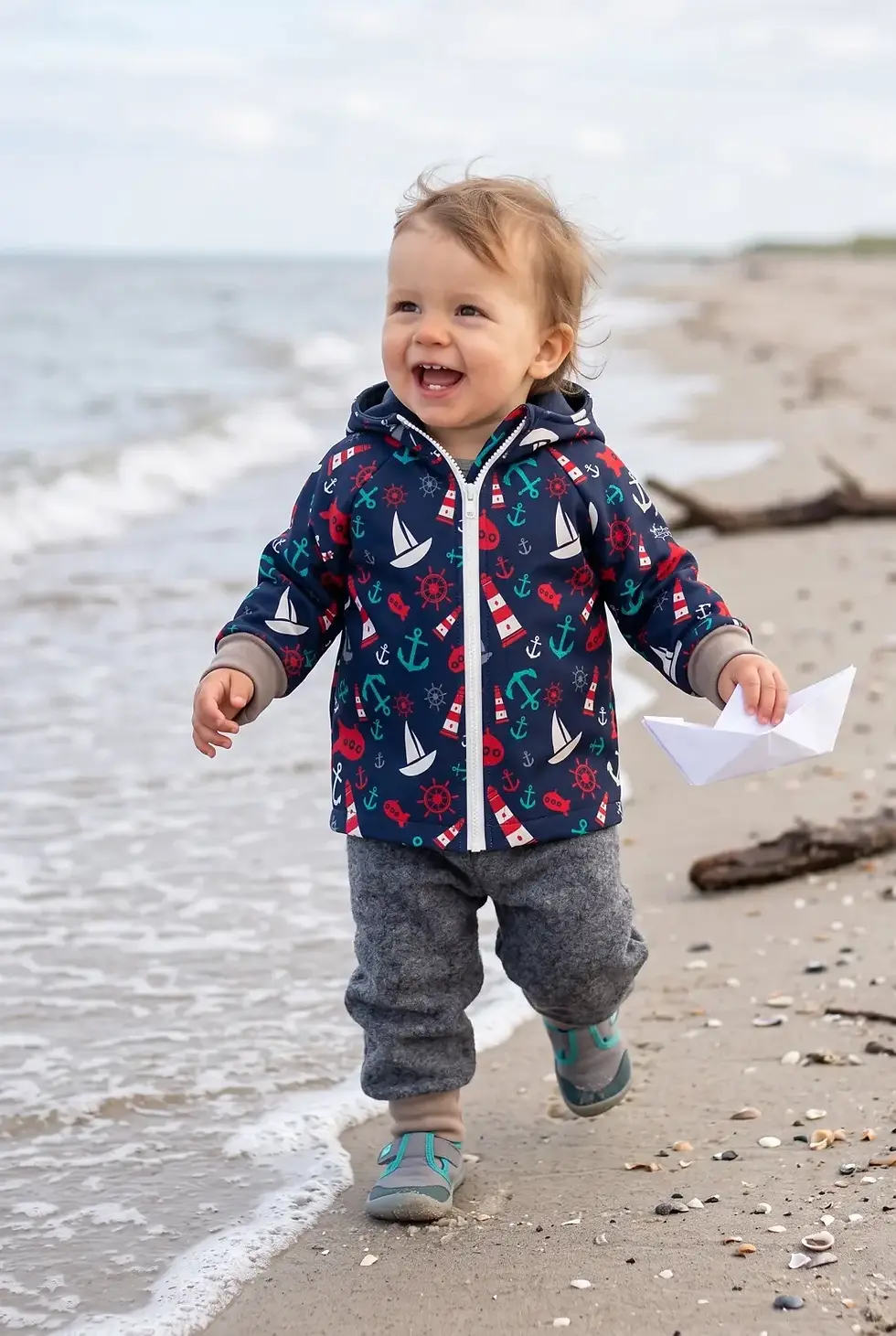 Kleinkind am Strand in gemusterter Jacke und dunkelgrau melierter Walkhose aus Wolle von Küstenfieber.