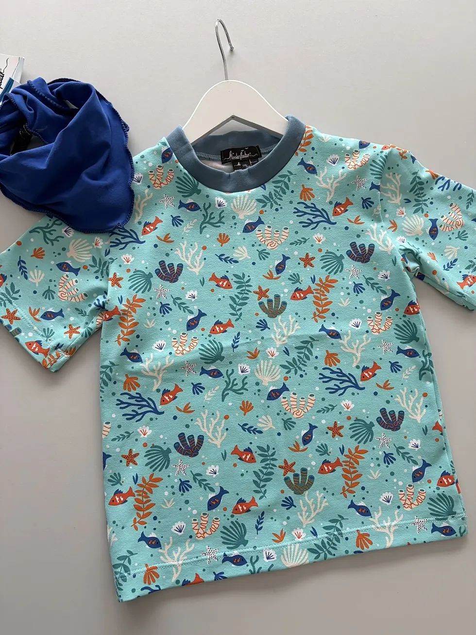 Miniaturbild: Kind trägt maritimes Kurzarmshirt mit Fischen und Korallen beim Lesen, weich, bequem und aus OEKO-TEX Baumwolle, handgemacht