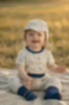 Baby trägt Musselin Sommer-Cap „Küstenfische“ in Creme mit maritimem Fischmuster. Leichter, atmungsaktiver Sonnenschutz für w