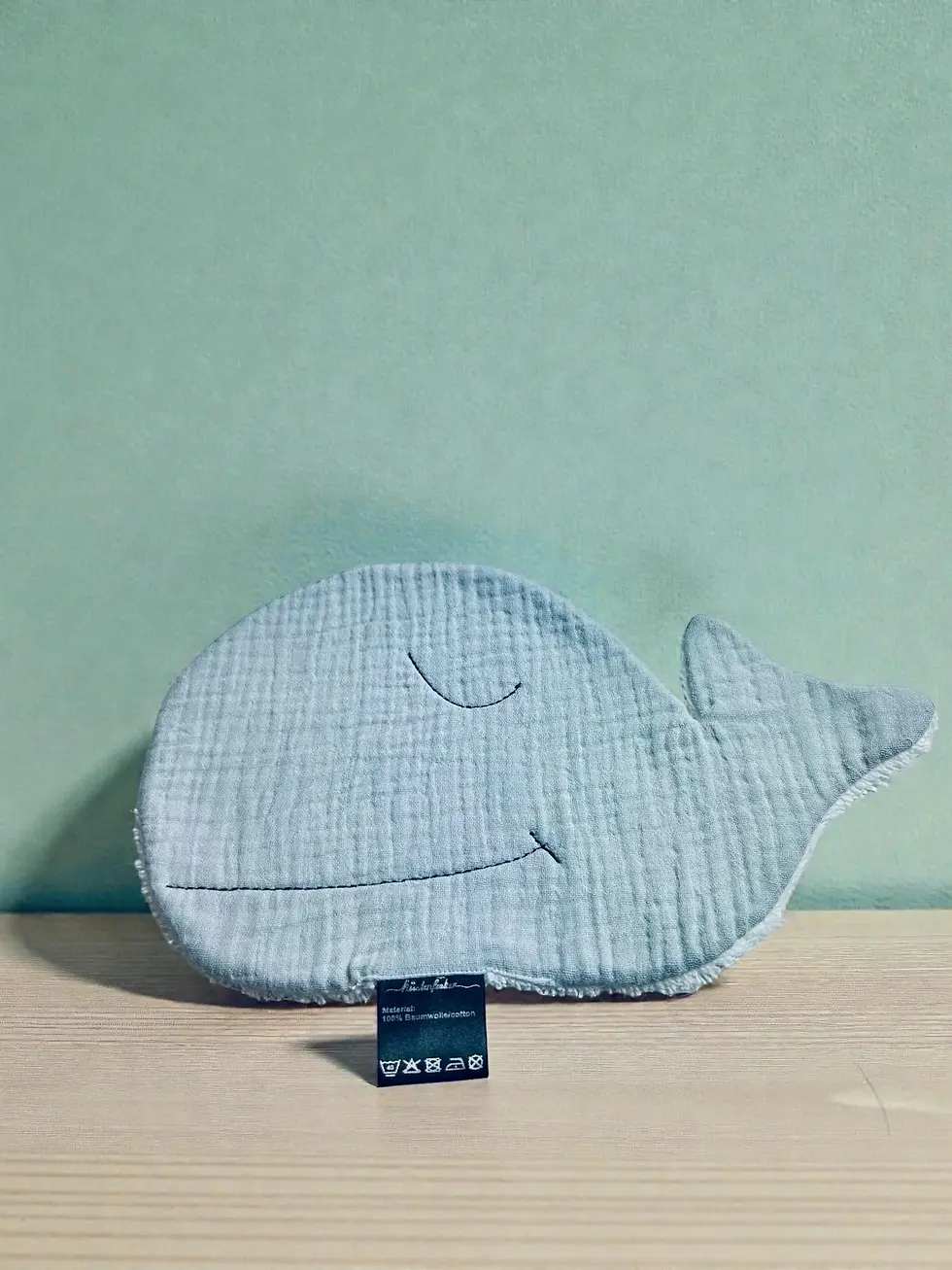 Miniaturbild: Minimalistisches Flatlay eines grauen Wal-Waschlappens aus Musselin. Zeitloses Babyaccessoire, handgemacht und vielseitig.