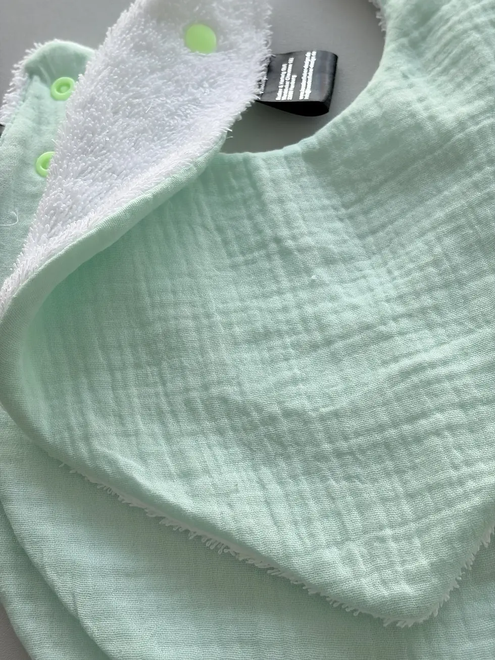 Miniaturbild: Detailaufnahme eines mintfarbenen Baby Lätzchens aus Musselin mit weicher Struktur und saugfähigem Frottee, perfekt für den A