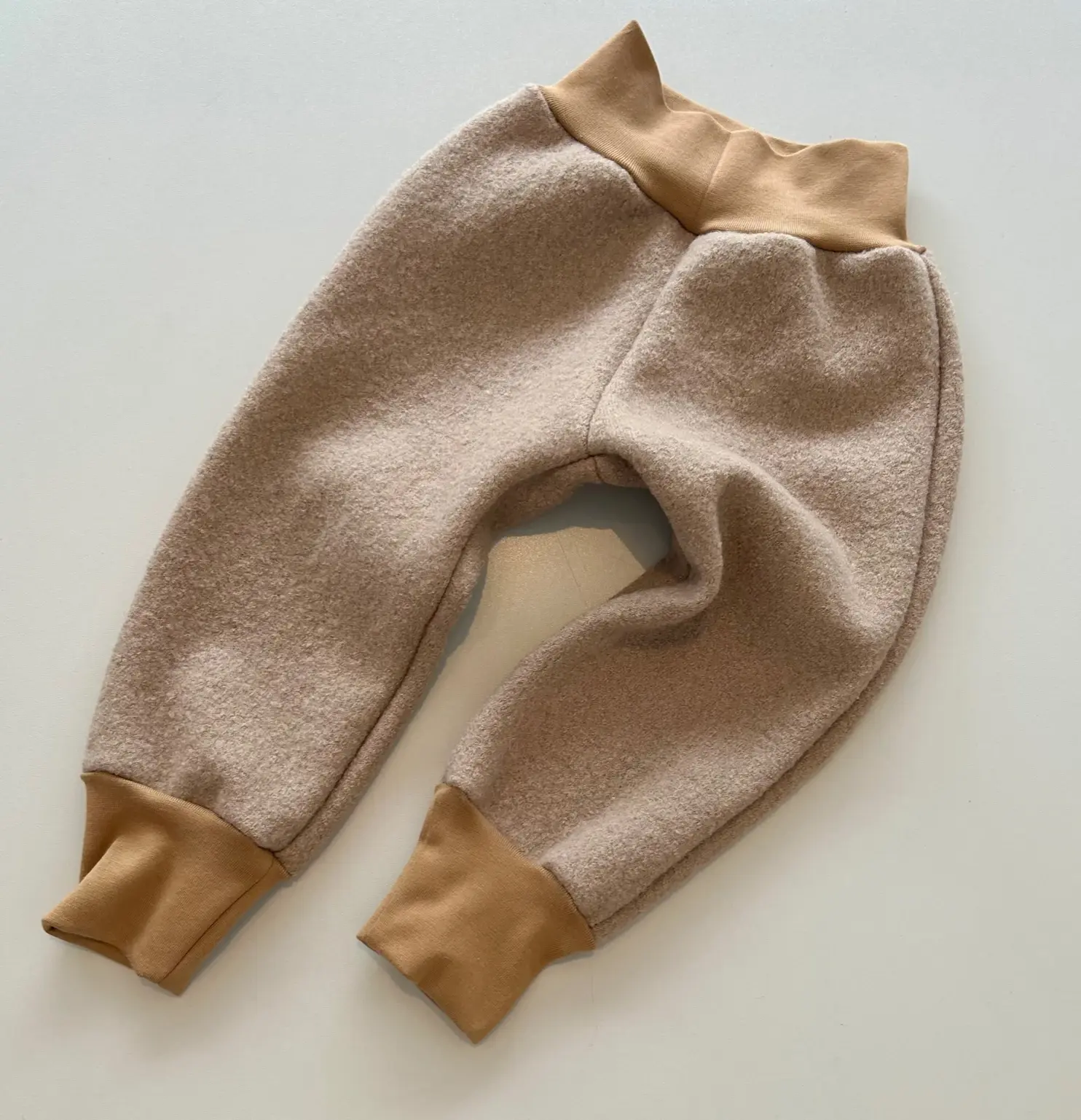 Baby trägt mitwachsende Walkhose in Camel – ideal für den Herbst, robust, winddicht & handgefertigt aus Schurwolle.